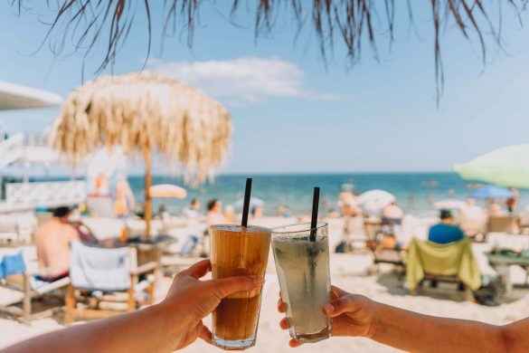 Cold drinks held up on a sunny beach with parasols
