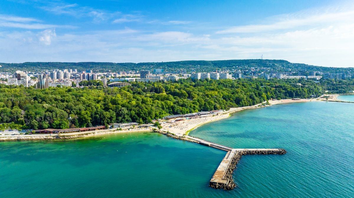 Coastline with a beach, a pier and a green park above turquoise water