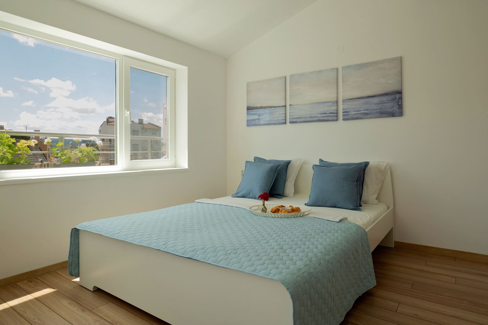 Bed with a blue bedspread, breakfast tray and a bright window