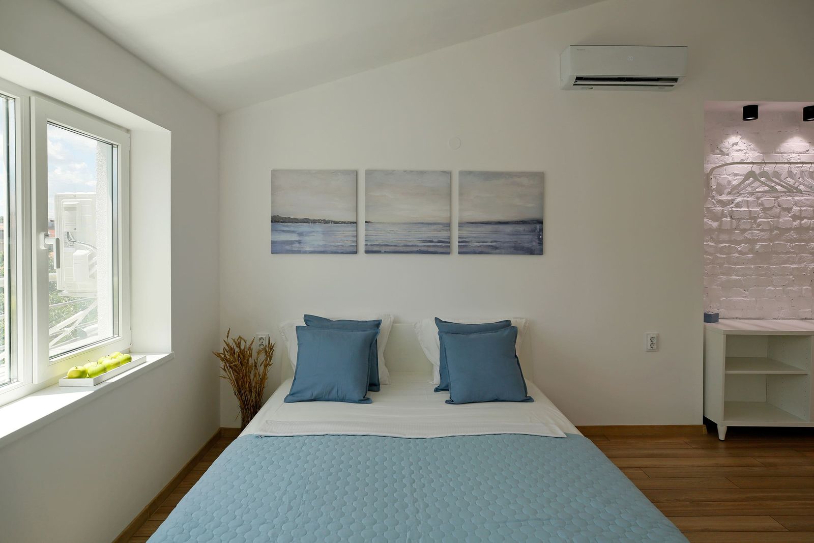 Double bed with blue cushions under three sea paintings